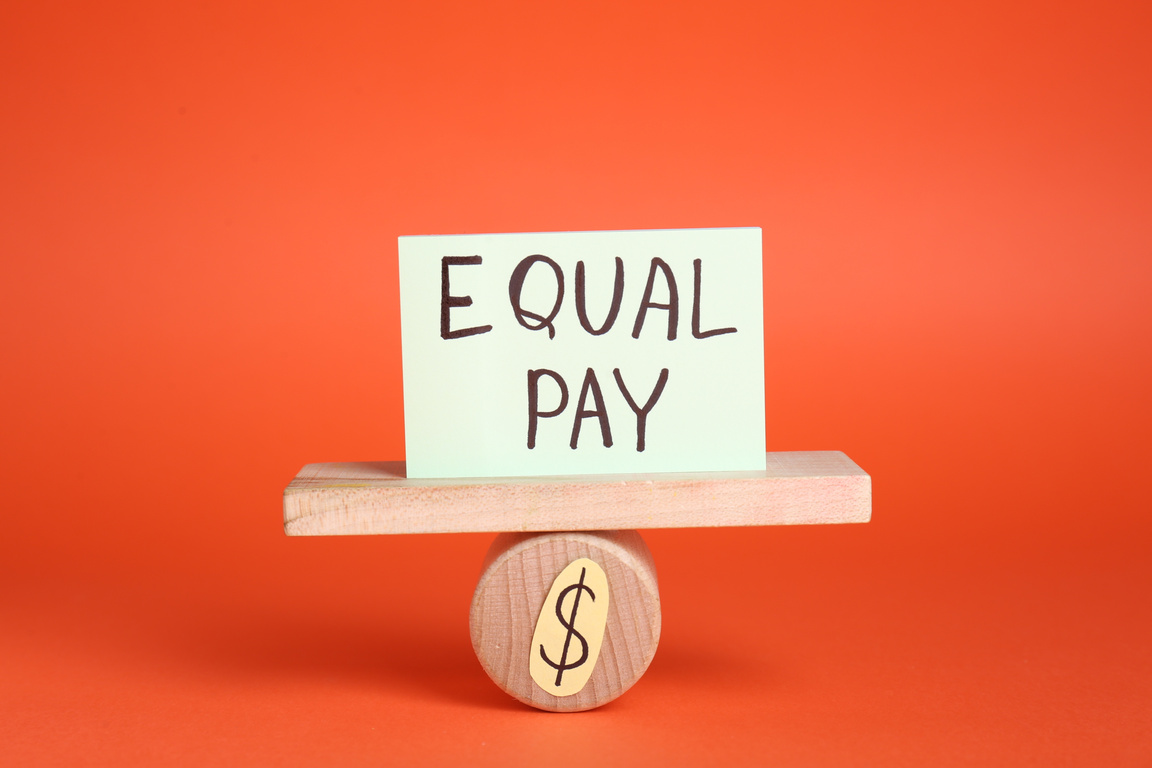 Equal Pay Concept. Paper Note on Miniature Seesaw against Red Background